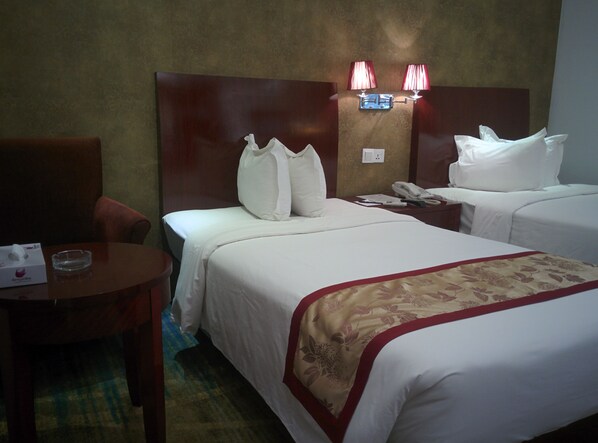 A hotel room with two beds, a bedside table with a telephone, and a chair.