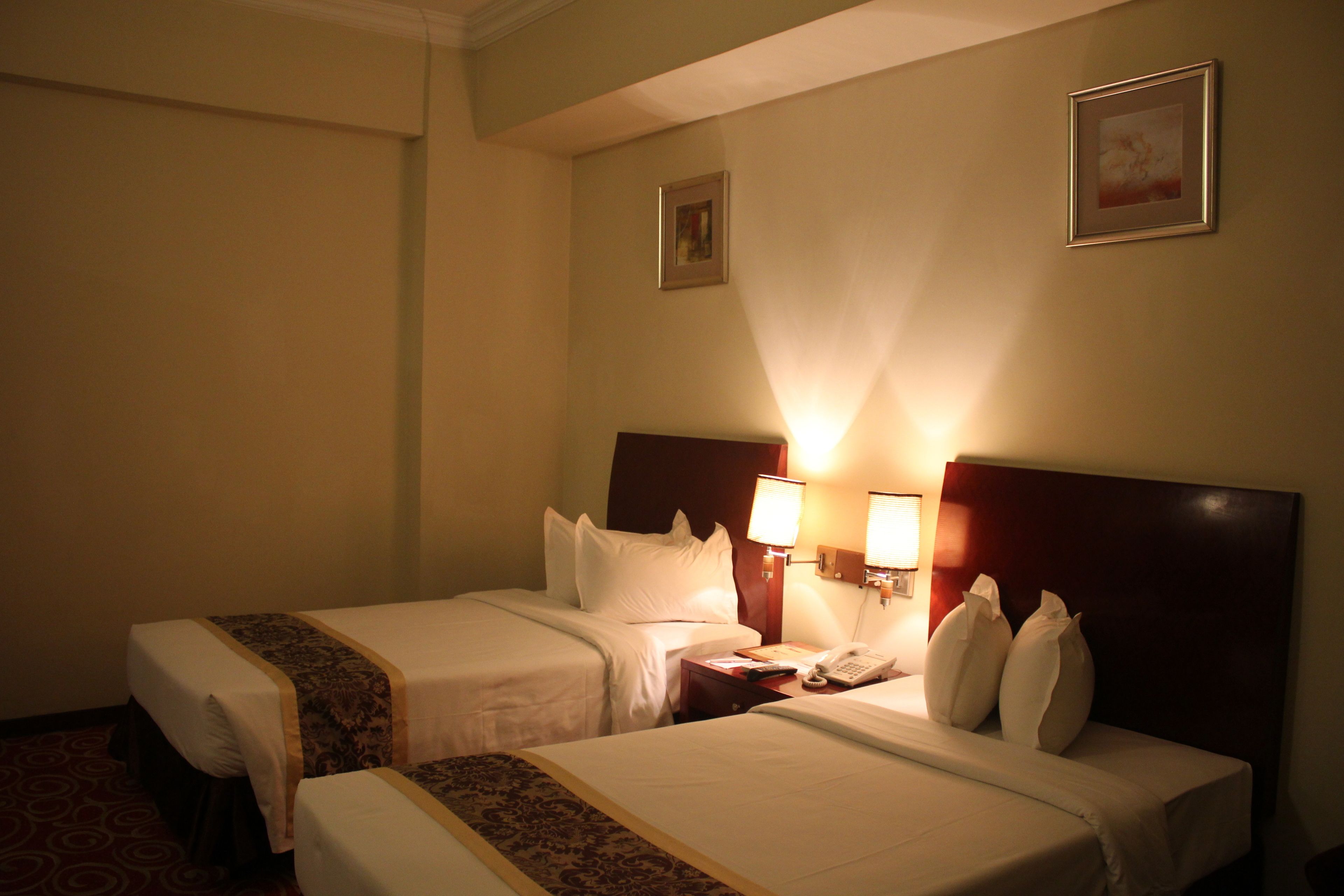 A hotel room with two beds, each with a headboard and bedside lamps.