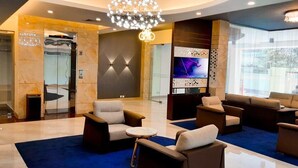 Un vestíbulo moderno con alfombra azul, zona de estar con sofás y sillones, una araña y un televisor de pantalla grande.