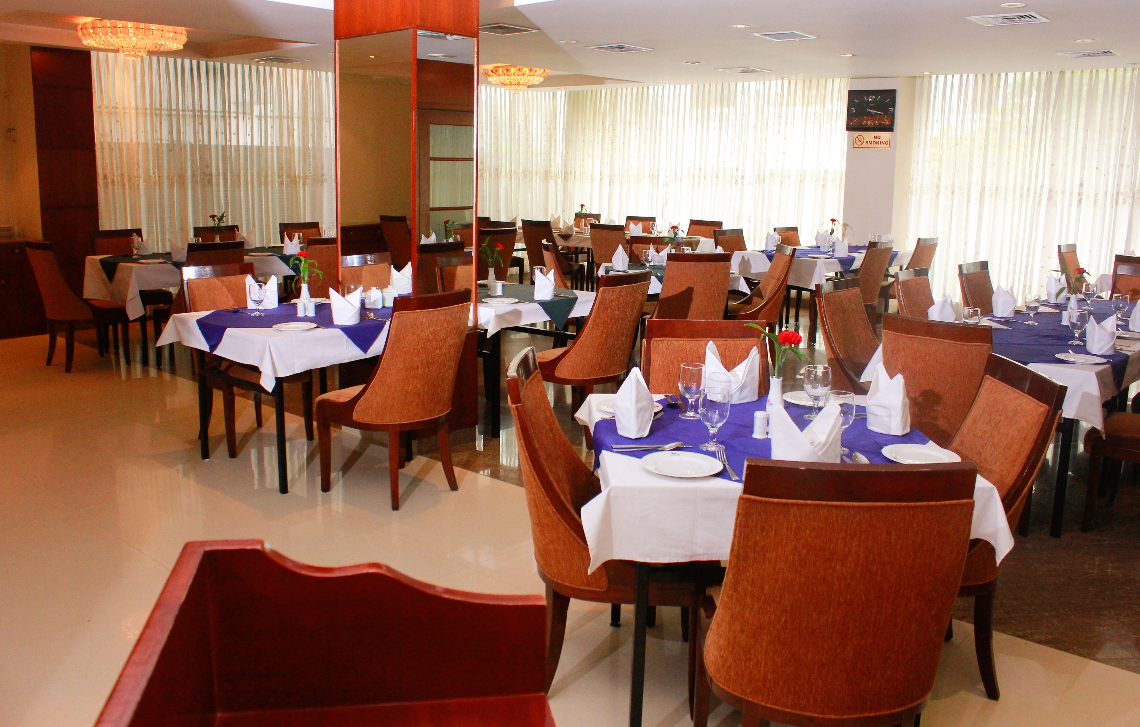 A restaurant with multiple tables set for dining, featuring white tablecloths and brown chairs.