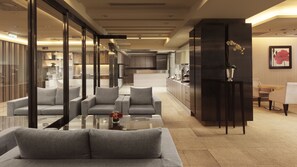 Eine moderne Hotelhalle mit Sitzgelegenheiten, einer Küche im Hintergrund und einer Zimmerpflanze auf einem Tisch.