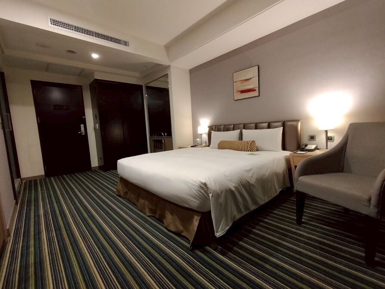 A hotel room with a large bed, a chair, a desk, and a nightstand.