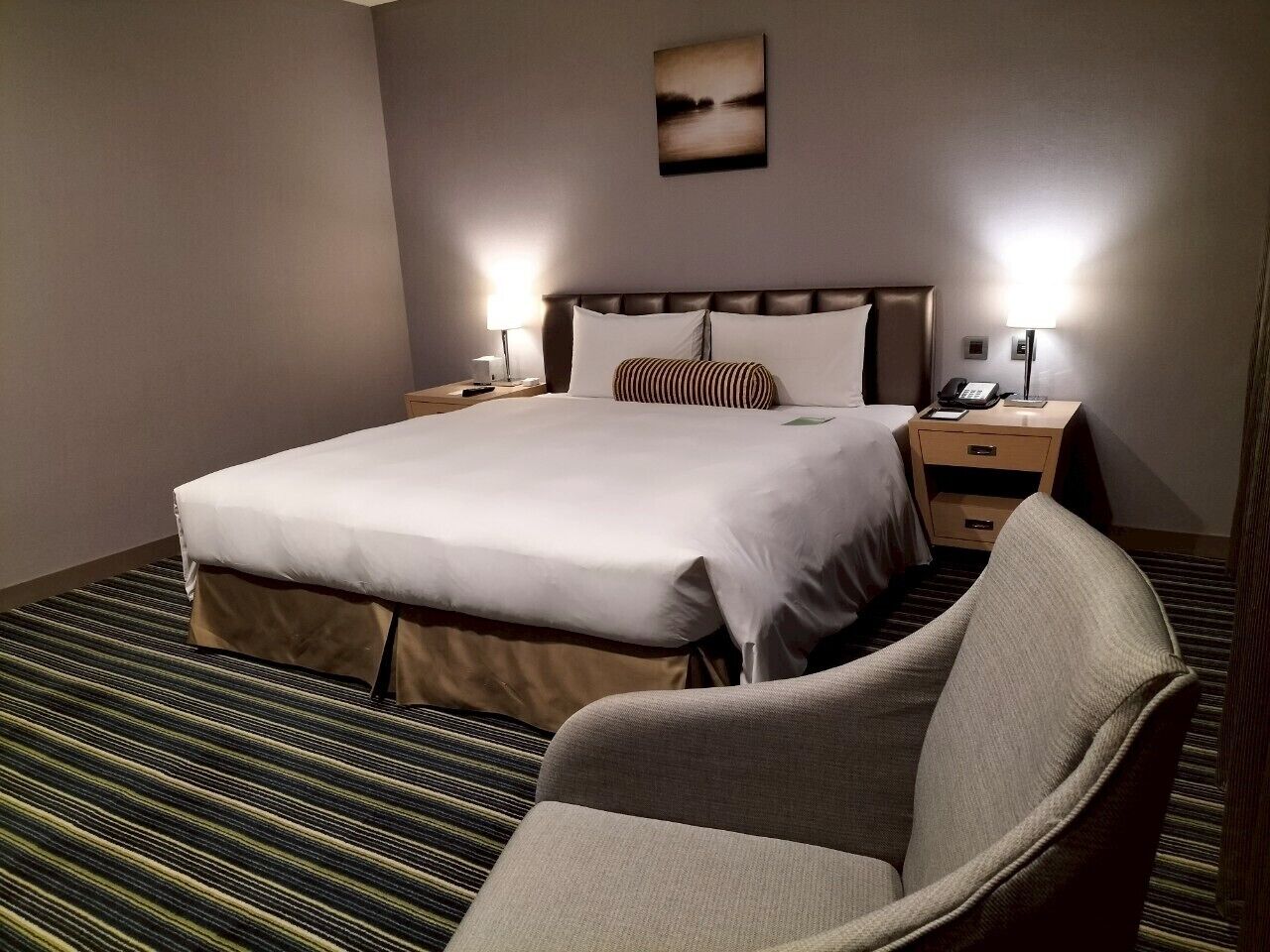 A hotel room with a large bed, two bedside tables, a chair, and a view of a body of water.