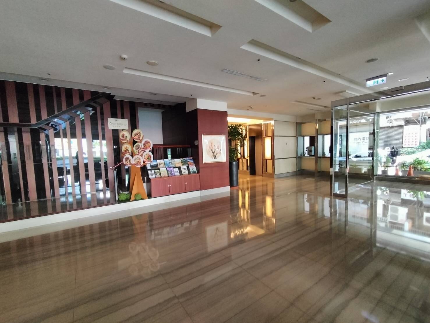 A spacious lobby with a polished floor, a staircase with a striped railing, and a display of books and magazines.
