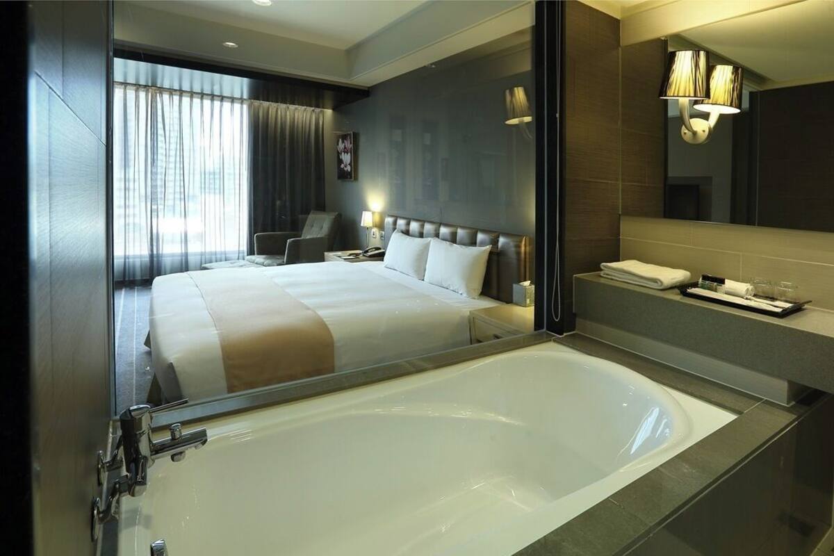 Ett modernt hotellrum med ett stort badkar, en säng med en sänggavel, ett skrivbord och en stol.