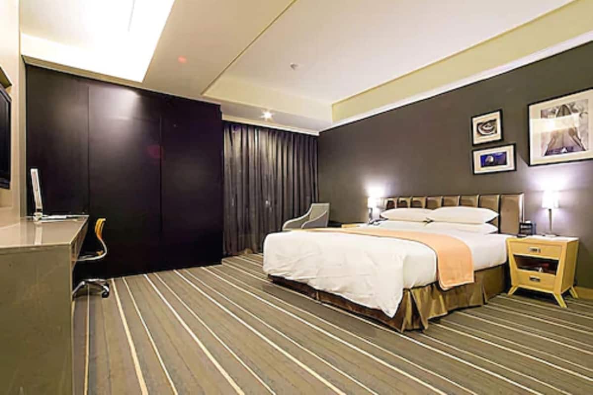 Ett hotellrum med en säng, ett skrivbord, en stol, en garderob och ett sängbord med en lampa.