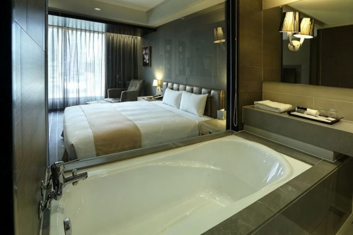 A modern hotel room with a large bed, a bathtub, a desk, and a mirror.