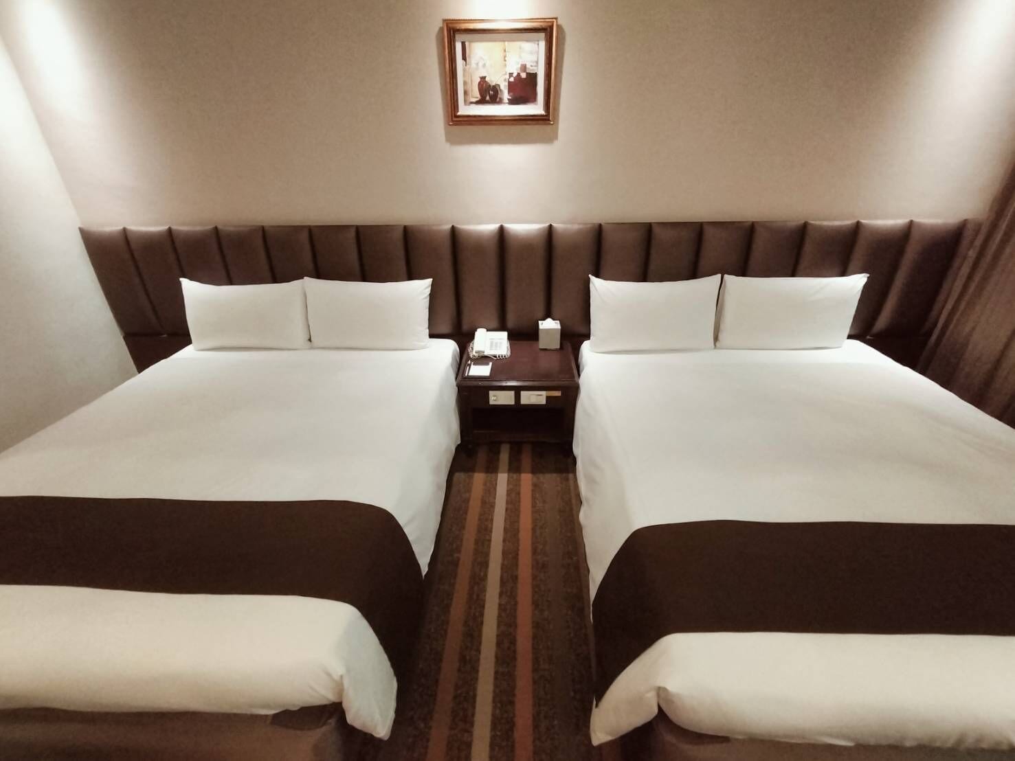 A hotel room with two beds, a nightstand, a framed picture on the wall, and a striped carpet.