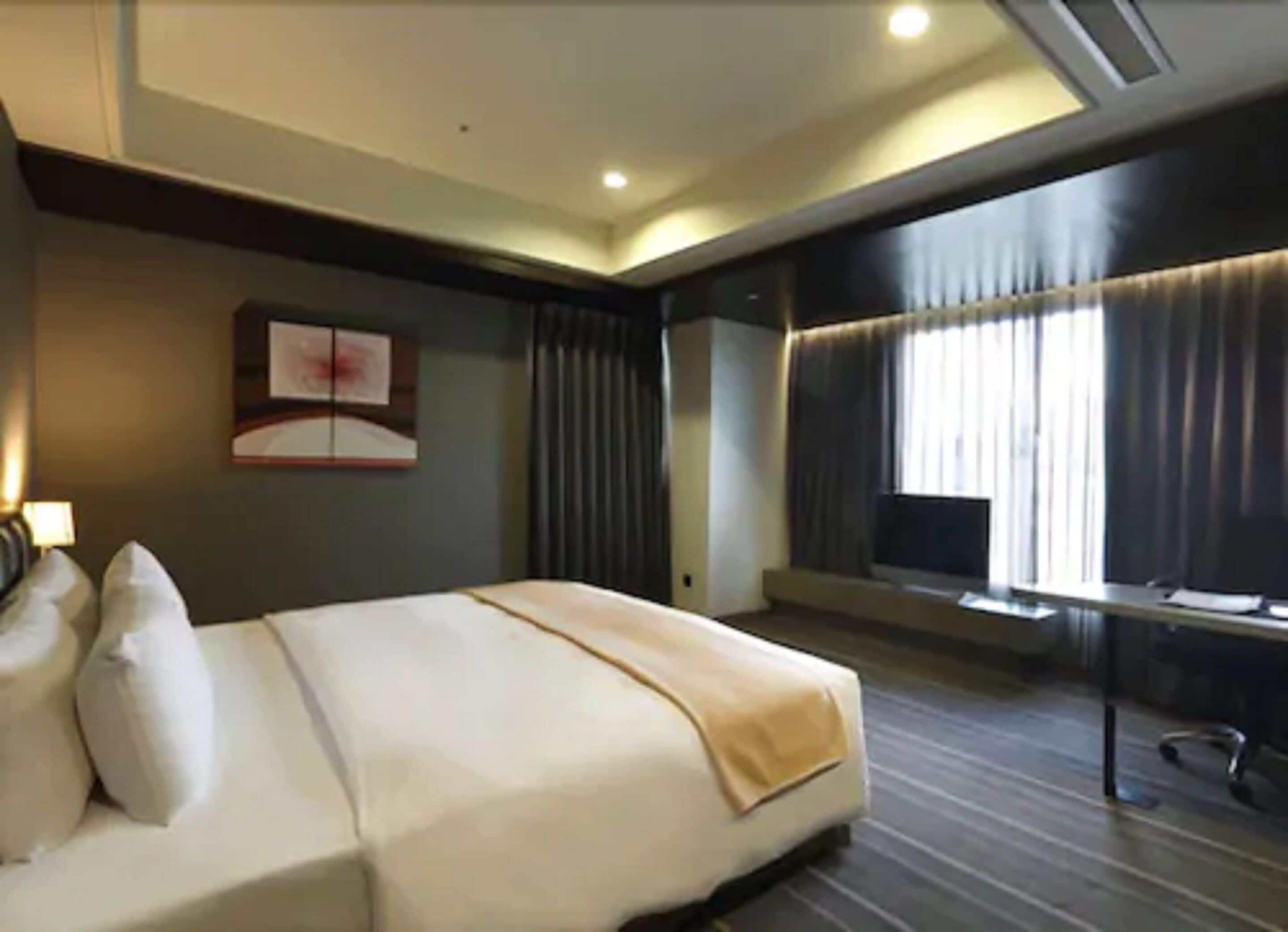 A hotel room with a large bed, a desk, and a window with curtains.
