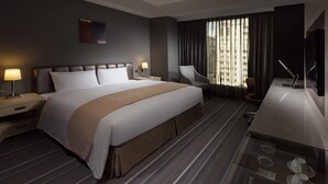 Una habitación de hotel con una cama grande, un escritorio con una computadora portátil, una silla y un televisor.