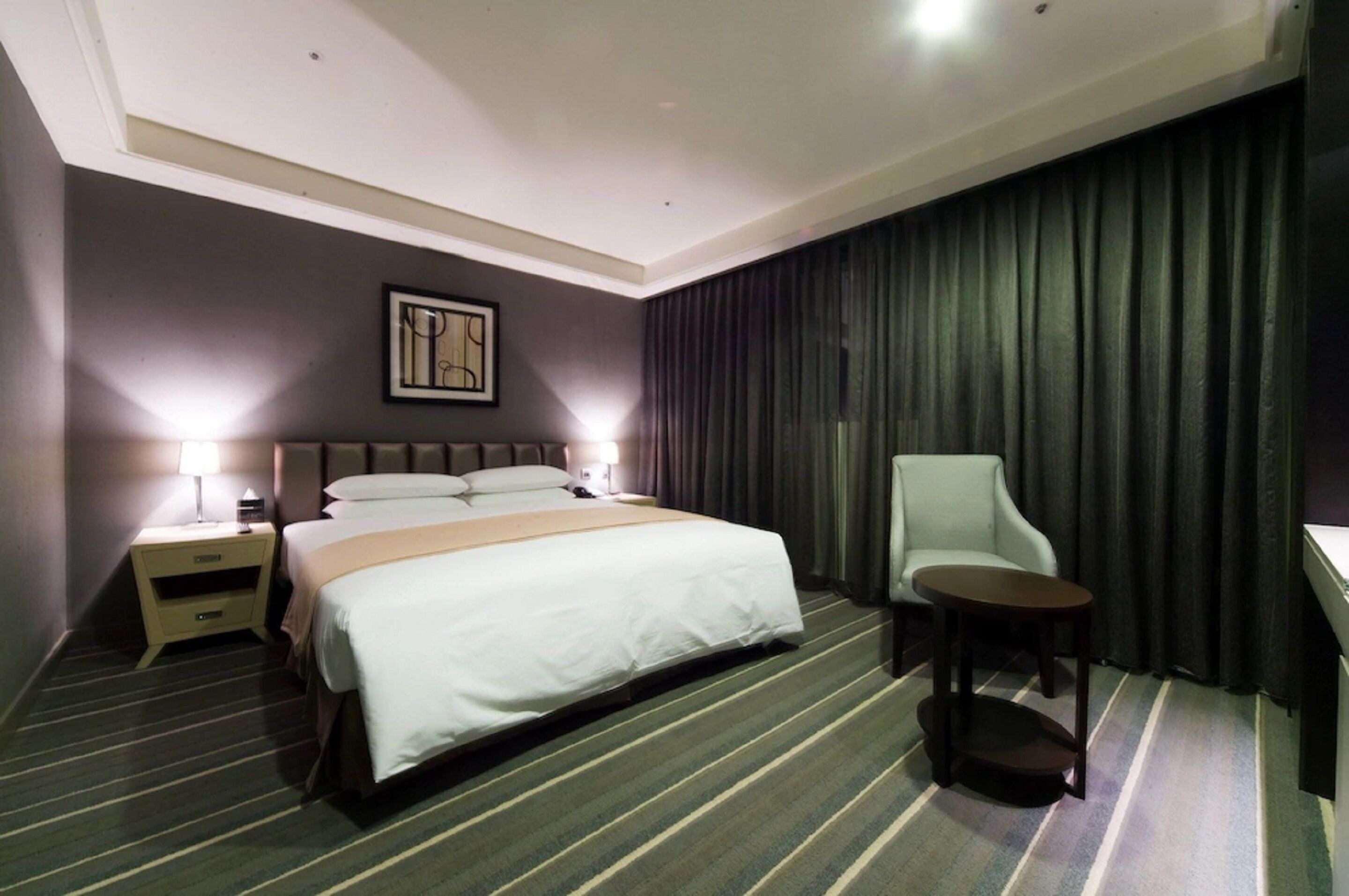 A hotel room with a large bed, bedside tables with lamps, a chair, and a small table.