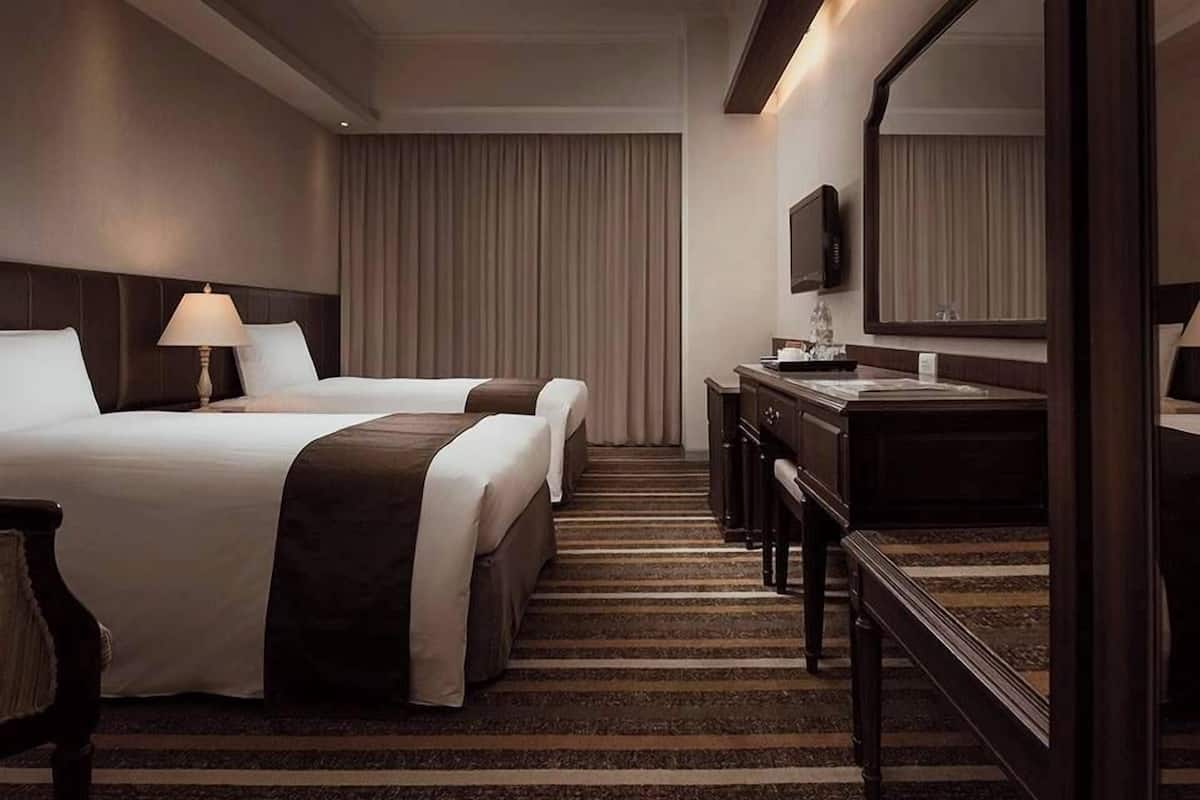 Ett hotellrum med två sängar, ett skrivbord, en stol, en spegel och en TV.