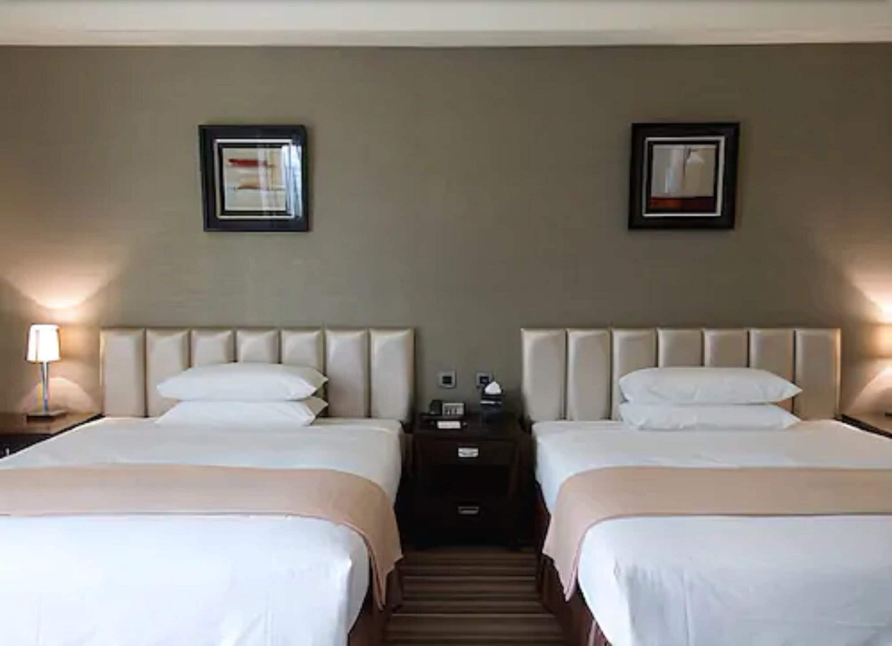 Una habitación de hotel con dos camas, una mesita de noche y una lámpara fijada a la pared.