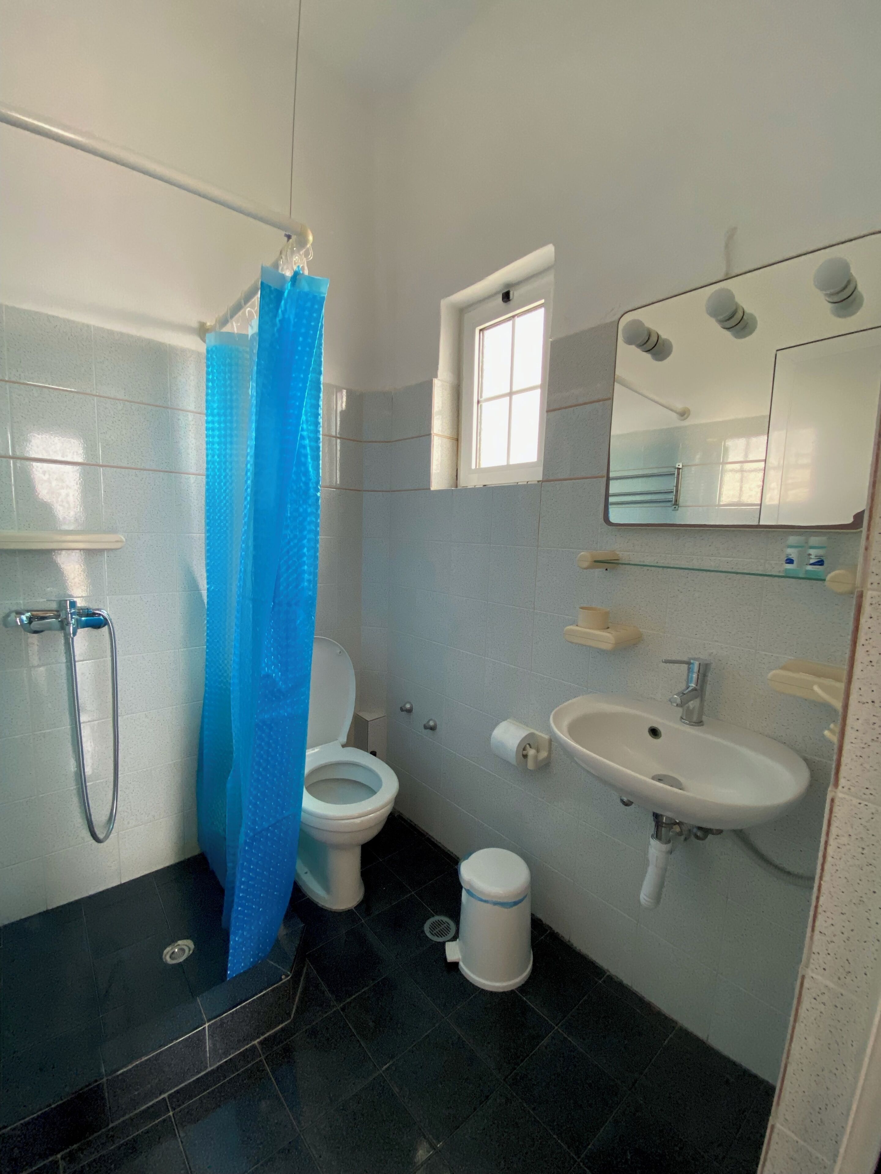 Un baño con ducha, inodoro, lavamanos y ventana.