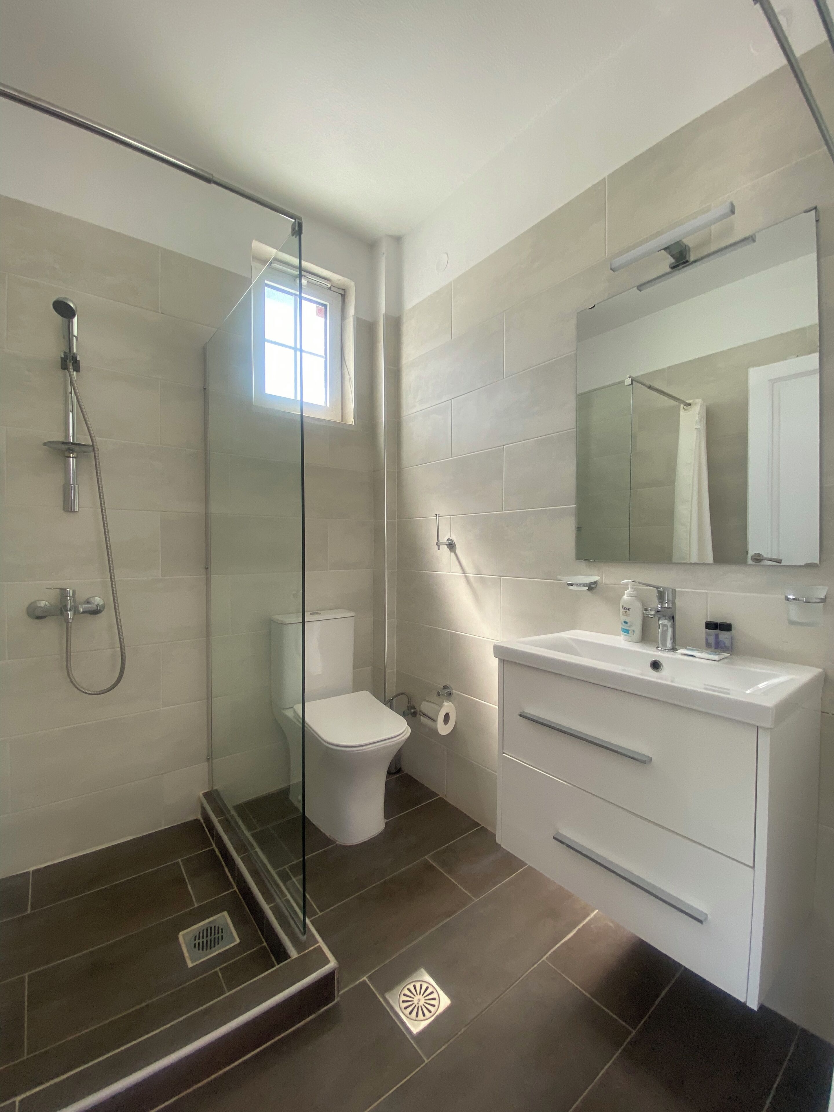 Une salle de bain moderne avec une douche à parois de verre, des toilettes blanches et un meuble-lavabo avec un miroir.
