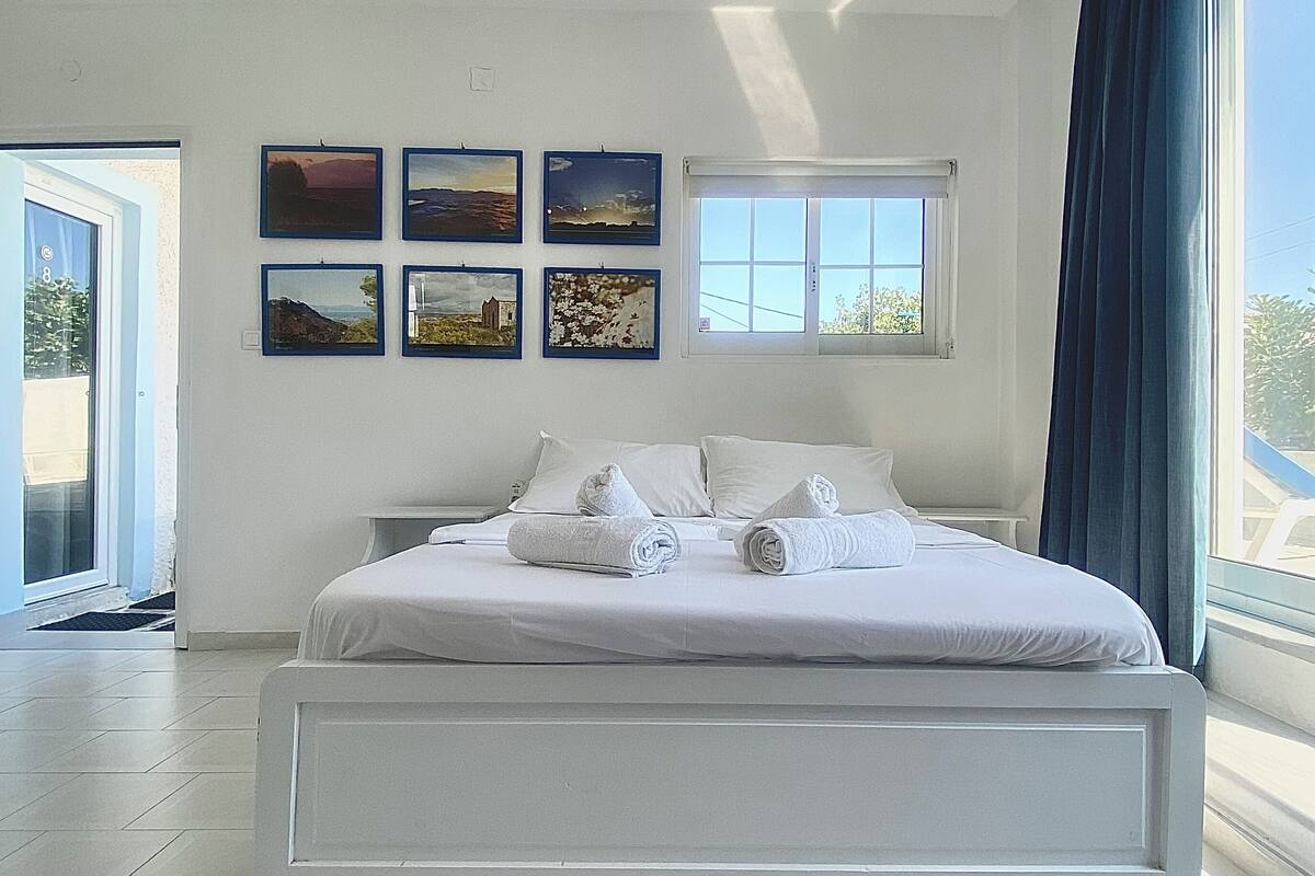 Een moderne slaapkamer met een groot bed, een raam met gordijnen, en zes ingelijste foto's aan de muur.