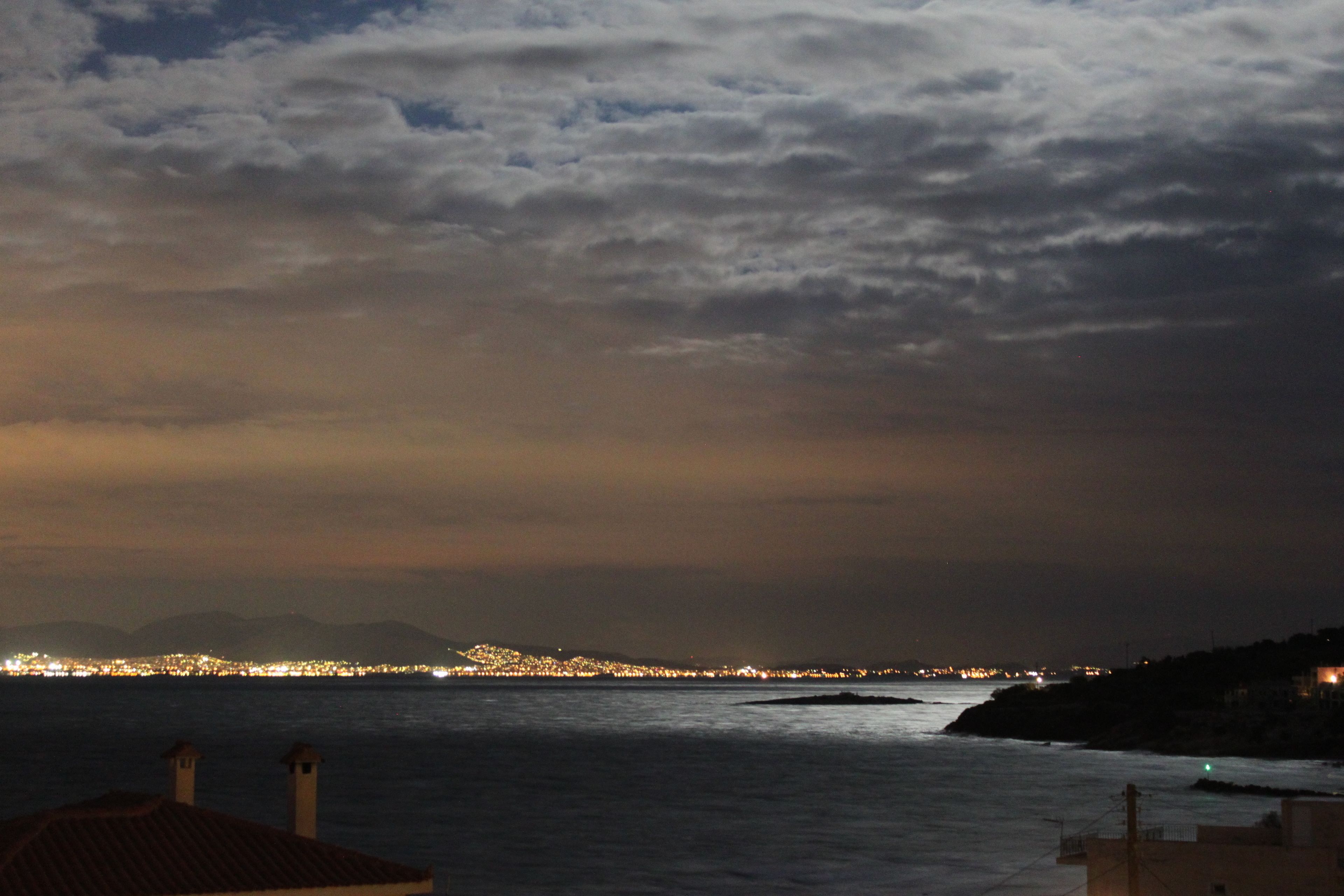 Un paisaje urbano costero al anochecer, con edificios a lo largo de la orilla y vista al mar.
