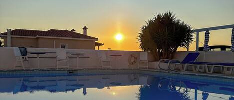 A swimming pool with a clear reflection of the sun and surrounding buildings during sunset.