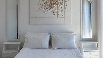 Una cama bien hecha con sábanas blancas y dos toallas enrolladas sobre un colchón blanco.