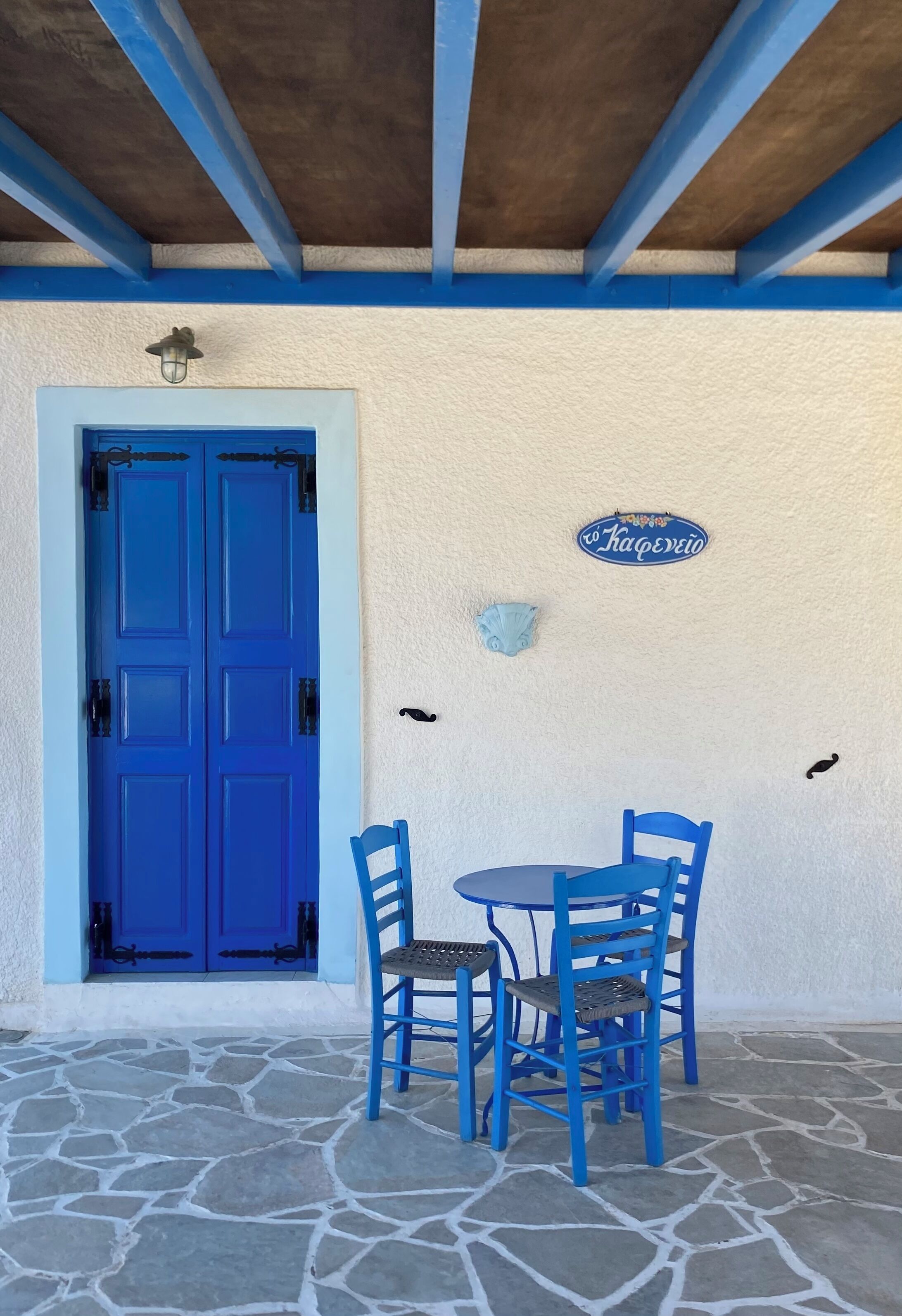 A blue door with a sign above it, a table with blue chairs, and a stone floor.