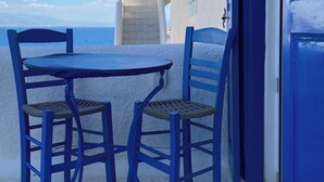 Una mesa y sillas azules en un patio de piedra con vistas al mar y edificios blancos.