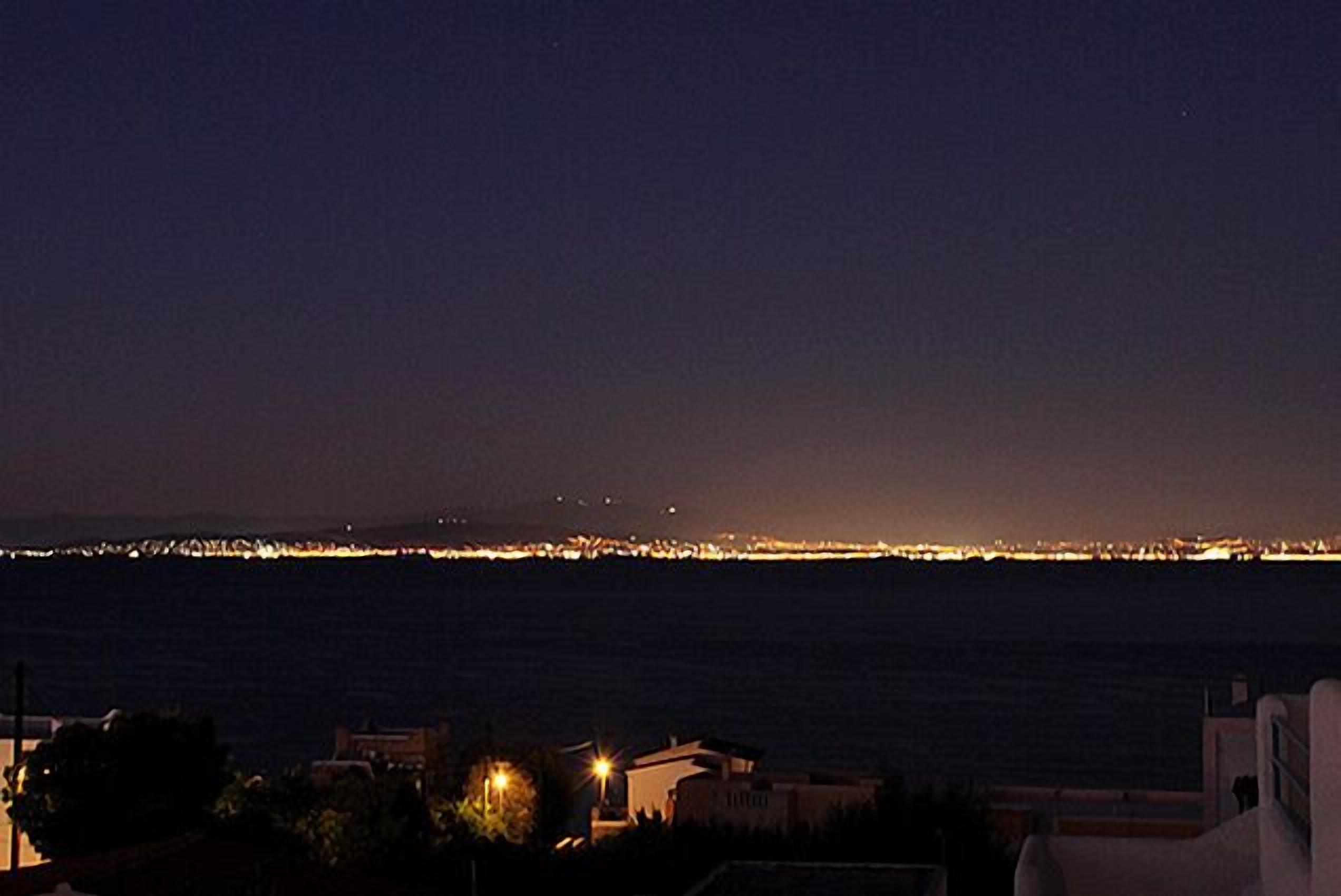 Vista costeira à noite com o horizonte da cidade ao longe.