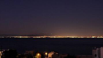 Vista costera nocturna con el horizonte de una ciudad a lo lejos.
