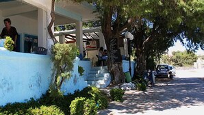 A building with a covered outdoor seating area, a tree, and a parked car. - Blue Dolphin Aegina (Aegina)