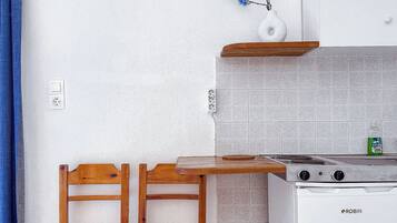 A compact kitchen with a white stove, two wooden chairs, a wooden table, and a blue curtain.