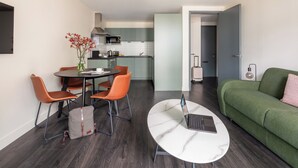 Ein modernes Wohnzimmer mit einem grünen Sofa, einem runden Couchtisch mit einem Laptop und einem Essbereich mit orangefarbenen Stühlen und einem Blumenvasen.