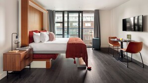 Ein modernes Hotelzimmer mit einem großen Bett, einem Schreibtisch, einem Stuhl, einem Fernseher und einem Balkon mit Blick auf die Stadt.