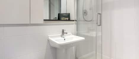 A modern bathroom with a white sink, a glass shower enclosure, and a mirror above the sink.