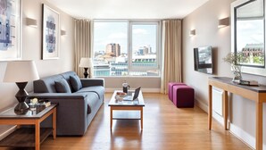 Un salon moderne avec un canapé, une table basse et un téléviseur. Une fenêtre offre une vue sur la ville.