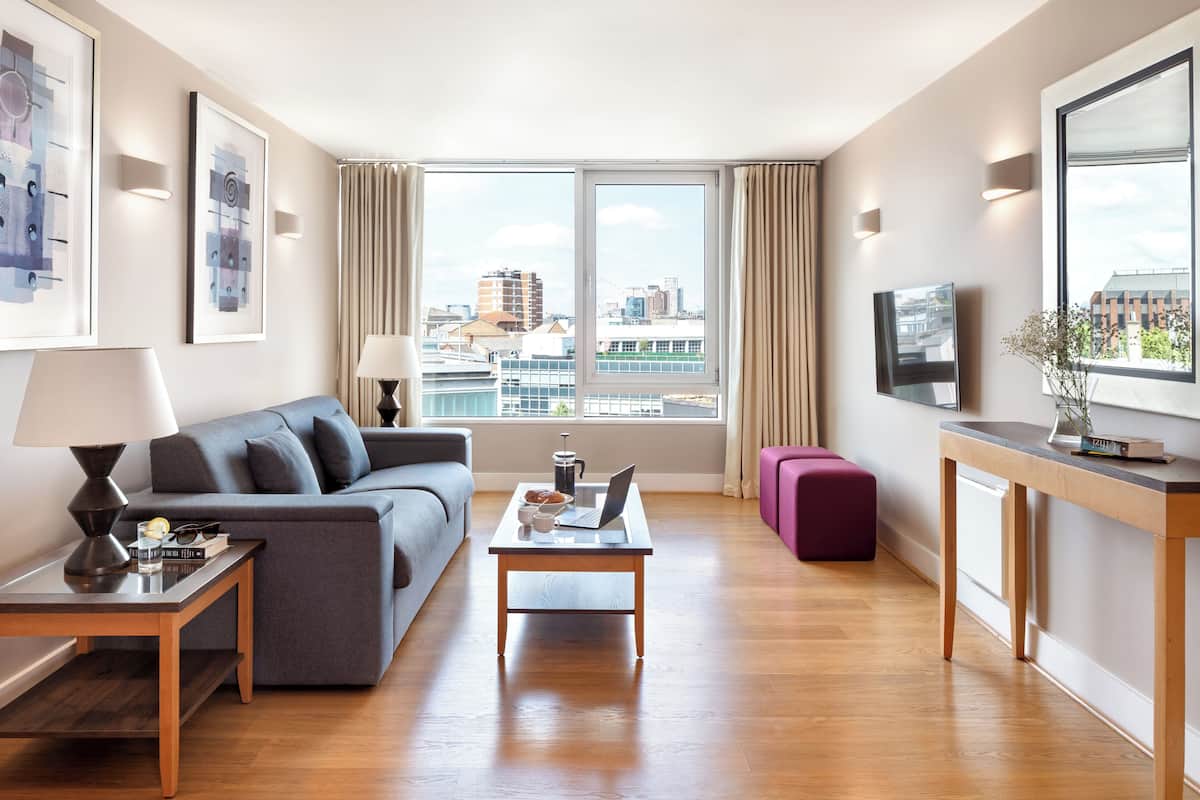 Ein modernes Wohnzimmer mit einer Couch, einem Couchtisch und einem Fernseher. Ein Fenster bietet Blick auf die Stadt.