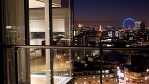 Un immeuble de grande hauteur, doté de larges fenêtres donnant sur une vue panoramique de la ville la nuit, avec notamment une structure circulaire illuminée qui se distingue.