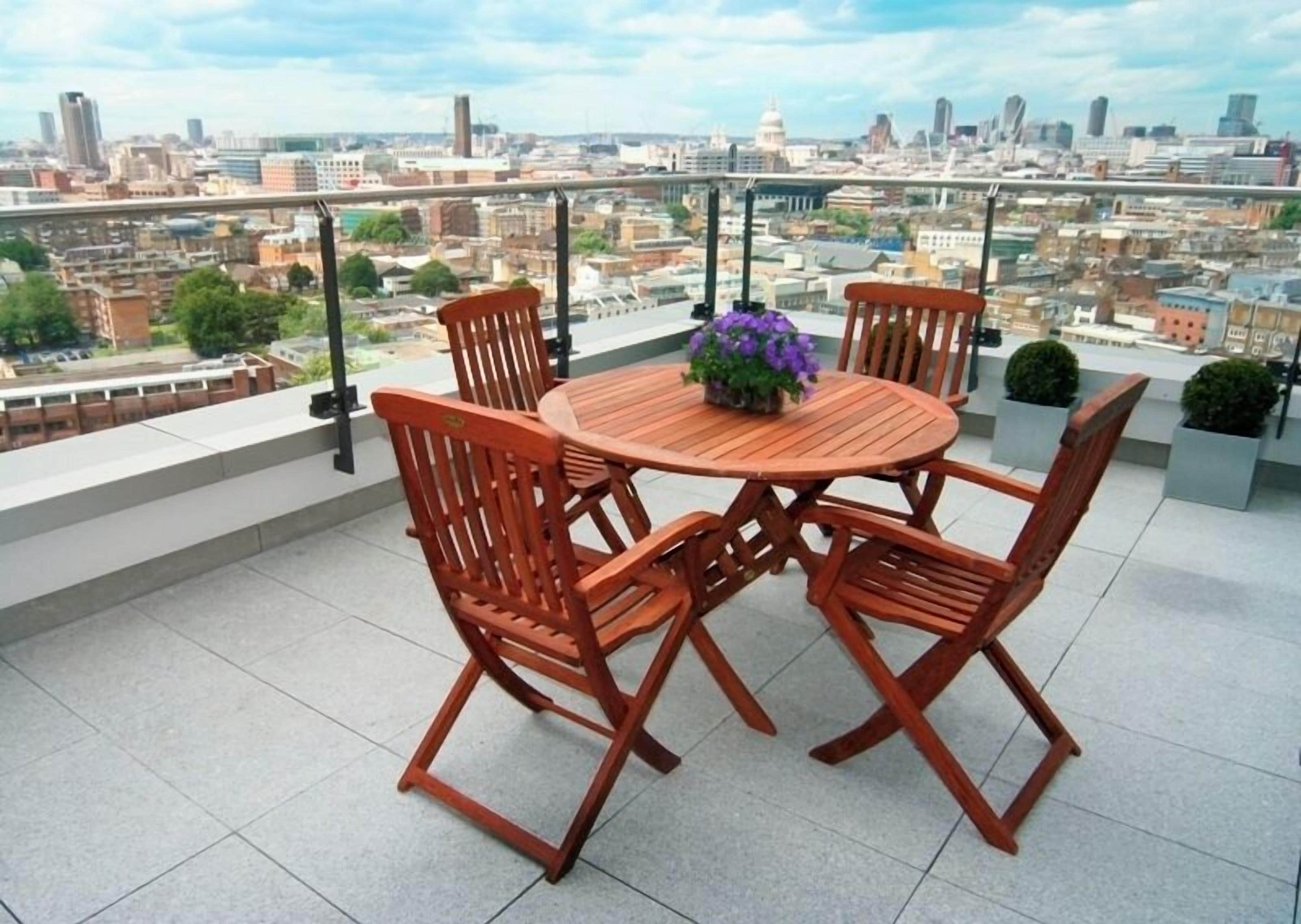 Une table ronde en bois, entourée de quatre chaises, et une plante en pot, le tout sur une terrasse sur le toit offrant une vue sur la ville.