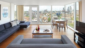 Un salon moderne comprenant un canapé, une table basse et un téléviseur, et offrant une vue sur la ville grâce à de grandes fenêtres.