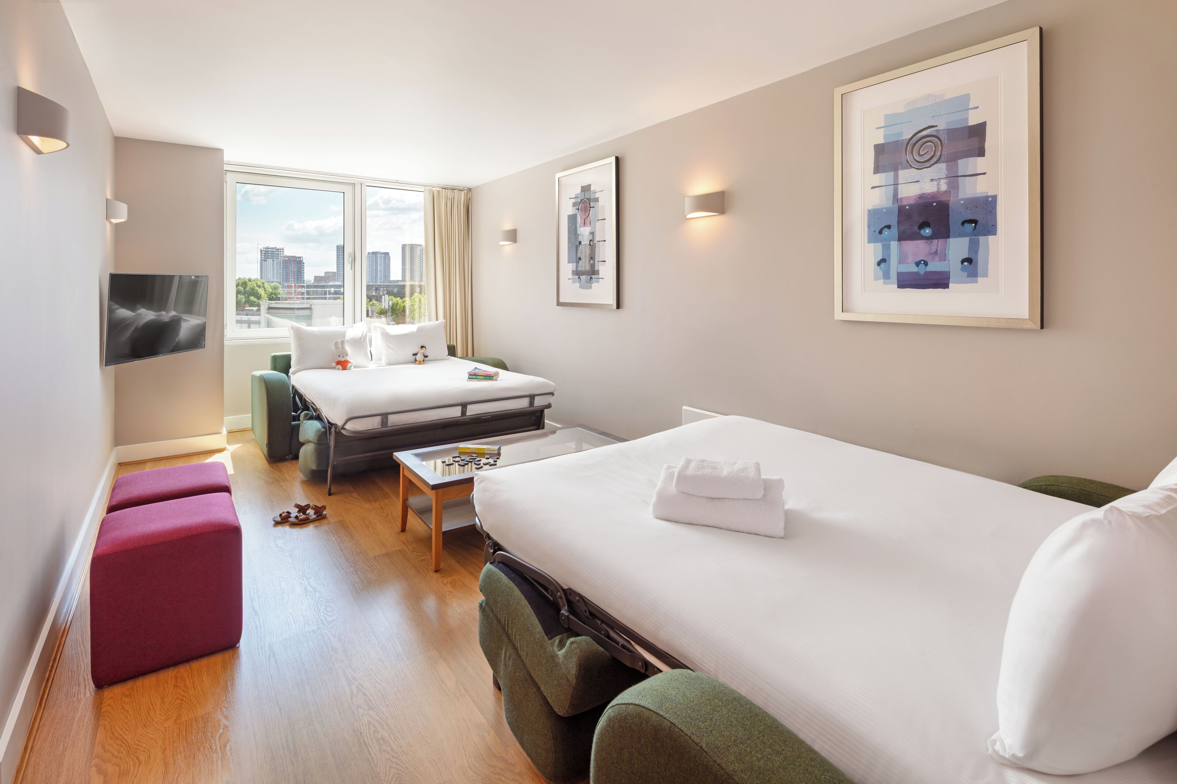 A modern hotel room with a large bed, a desk, and a view of the city.