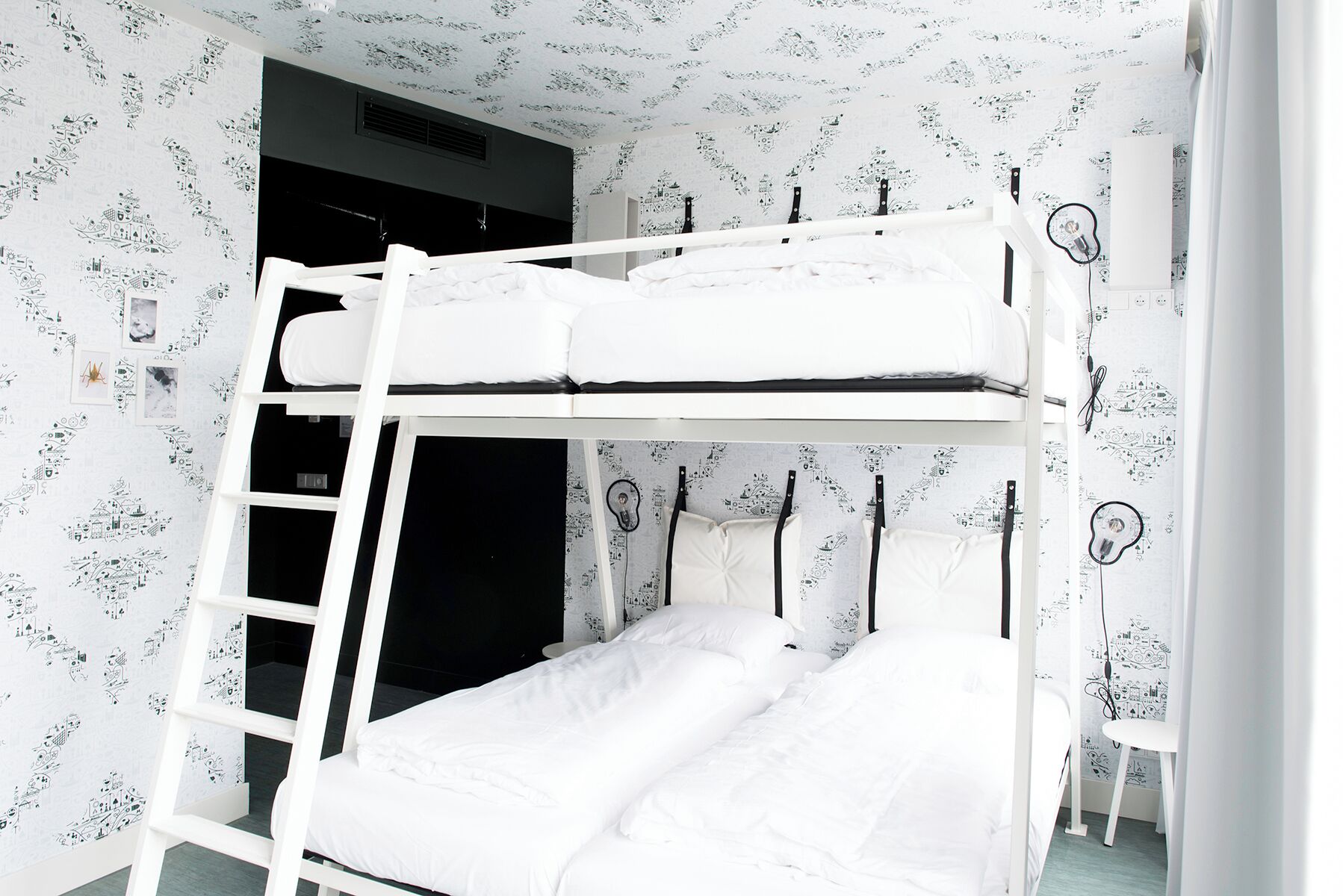 Une chambre avec un lit superposé, une échelle, du linge de lit blanc et un mur recouvert d’un papier peint à motifs.