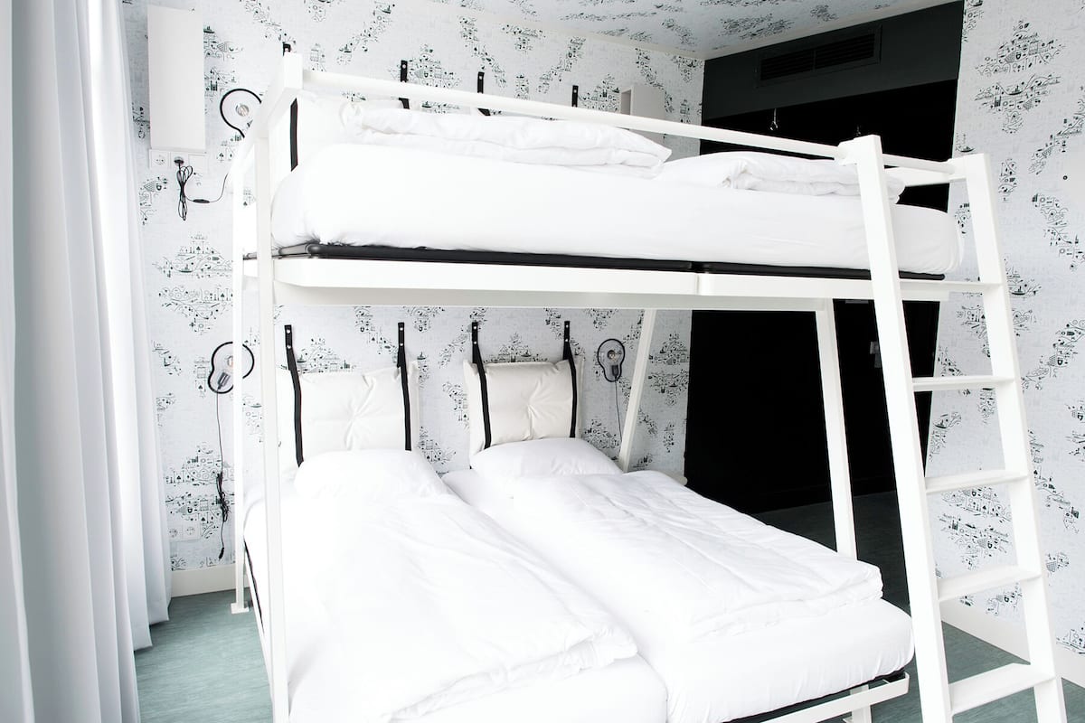 Ein Stockbett in einem Raum mit ornamentalem Wandpapier und einem Fenster.