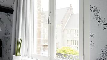 Ein Zimmer mit weißem Schreibtisch, einer Topfpflanze und einem Fenster mit Blick auf Gebäude.