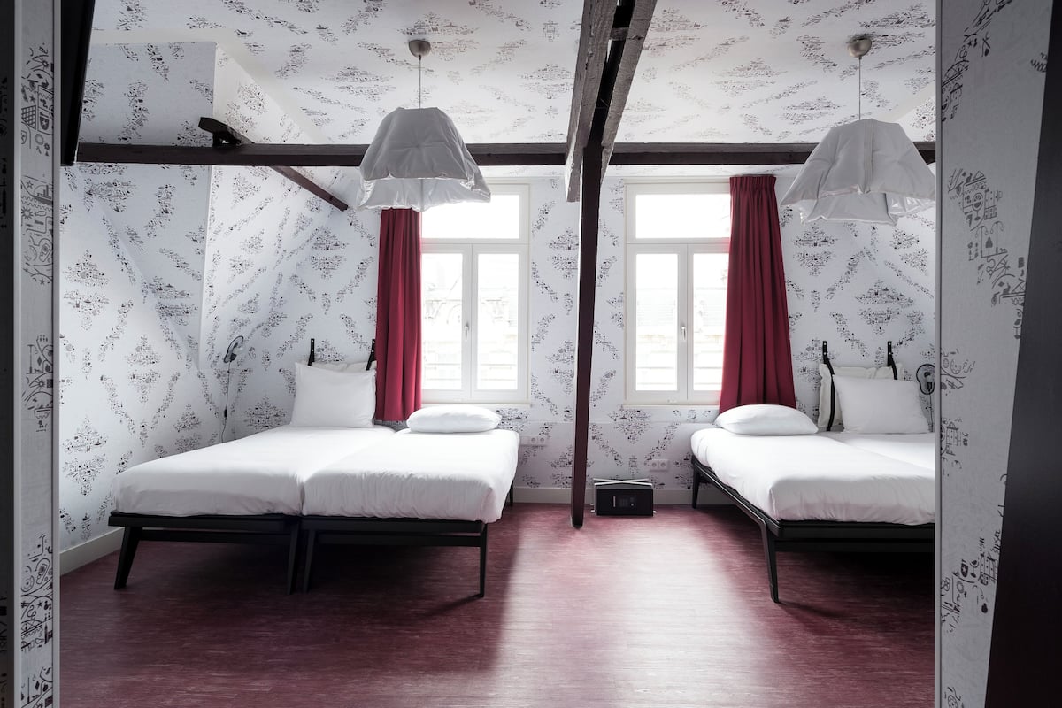 Ein Zimmer mit zwei Betten, Holzboden und Wandtapete mit Muster.