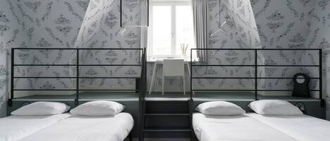 A dormitory room with bunk beds, a desk, and a window with curtains.