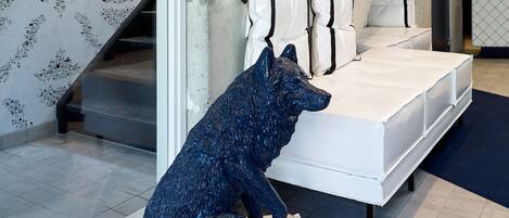 A room with a bed, a white pillow, a blue sculpture of a dog, and a staircase.