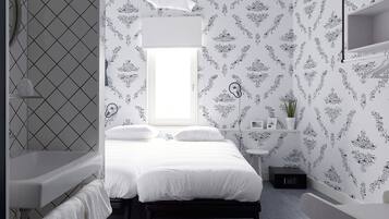 Un dormitorio moderno con una cama, una mesita de noche, una ventana pequeña y un baño a la izquierda.