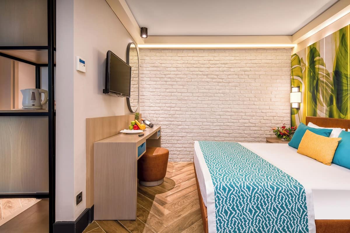 A hotel room with a bed, a desk with a chair, a TV, and a bookshelf.