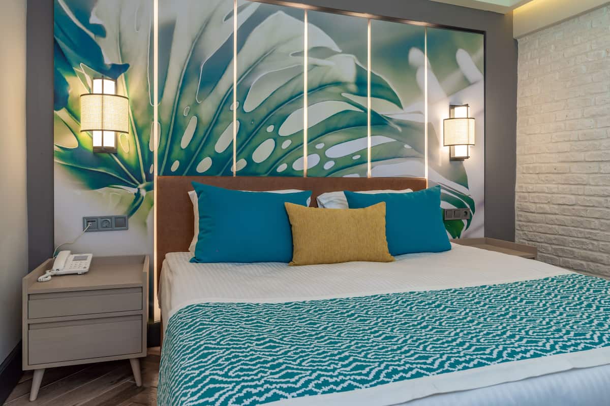 A hotel room with a large bed, a nightstand with a phone, and a wall with a leaf pattern.