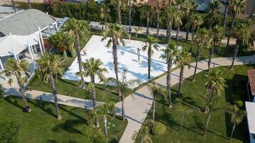 Vista aérea de un resort con una gran piscina rodeada de palmeras, un pabellón cubierto y un edificio con techo de tejas rojas.