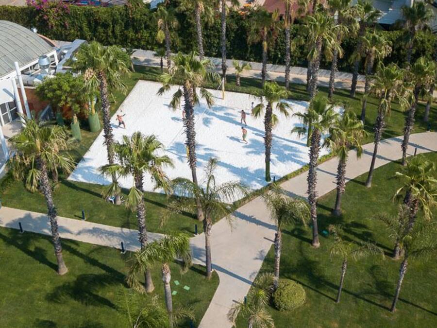 Vista aérea de un resort con una gran piscina rodeada de palmeras, un pabellón cubierto y un edificio con techo de tejas rojas.