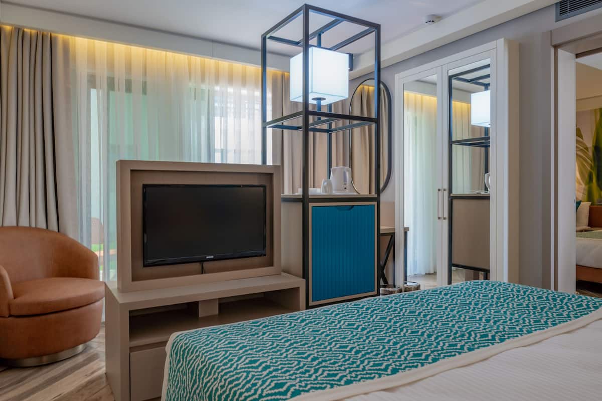 A hotel room with a bed, a TV, a seating area, and a bathroom visible through an open door.